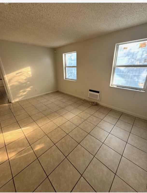An empty room with beige tile flooring, two windows, and a wall-mounted air conditioning unit — 720 NW 6th Avenue # 5, Pompano Beach FL 33060, POMPANO BEACH, FL