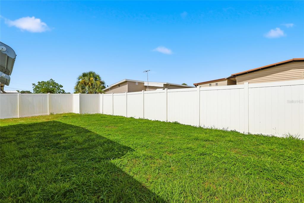 A grassy backyard is enclosed by a tall white vinyl privacy fence — 5417 AMANDA STREET, ZEPHYRHILLS, FL