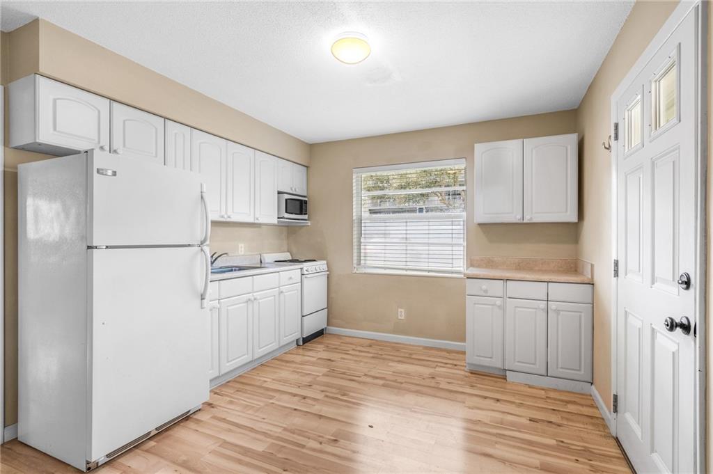 A kitchen with white cabinets, white appliances, light wood flooring, and a window — 919 Turtle Cove Lane, Vero Beach FL 32963, VERO BEACH, FL