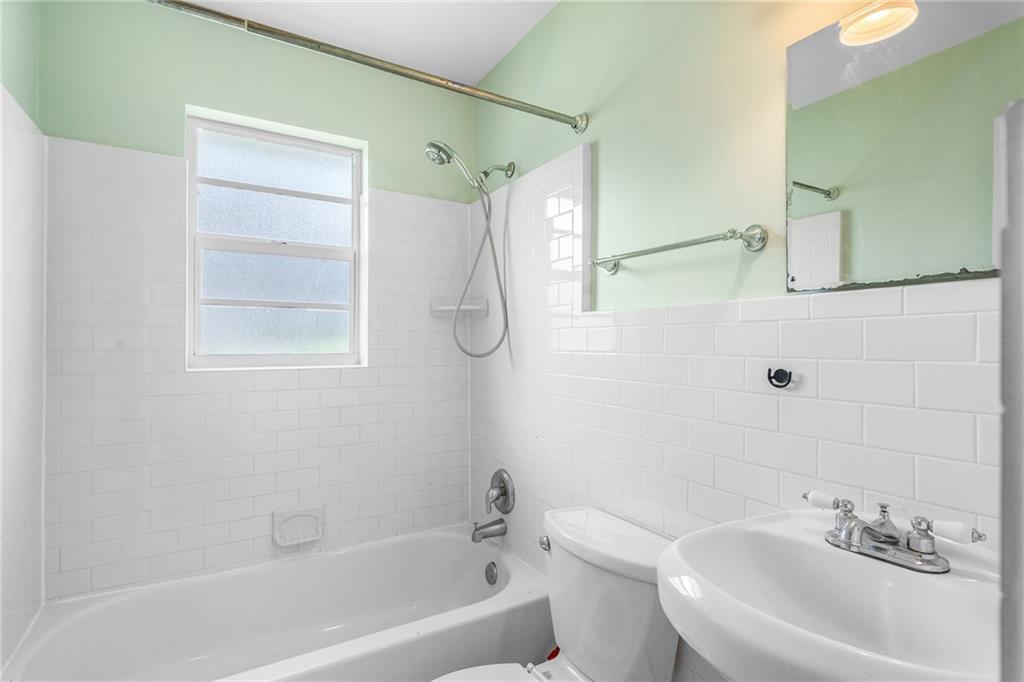 A bathroom features a white subway-tiled tub surround, a pedestal sink, and light green walls — 919 Turtle Cove Lane, Vero Beach FL 32963, VERO BEACH, FL