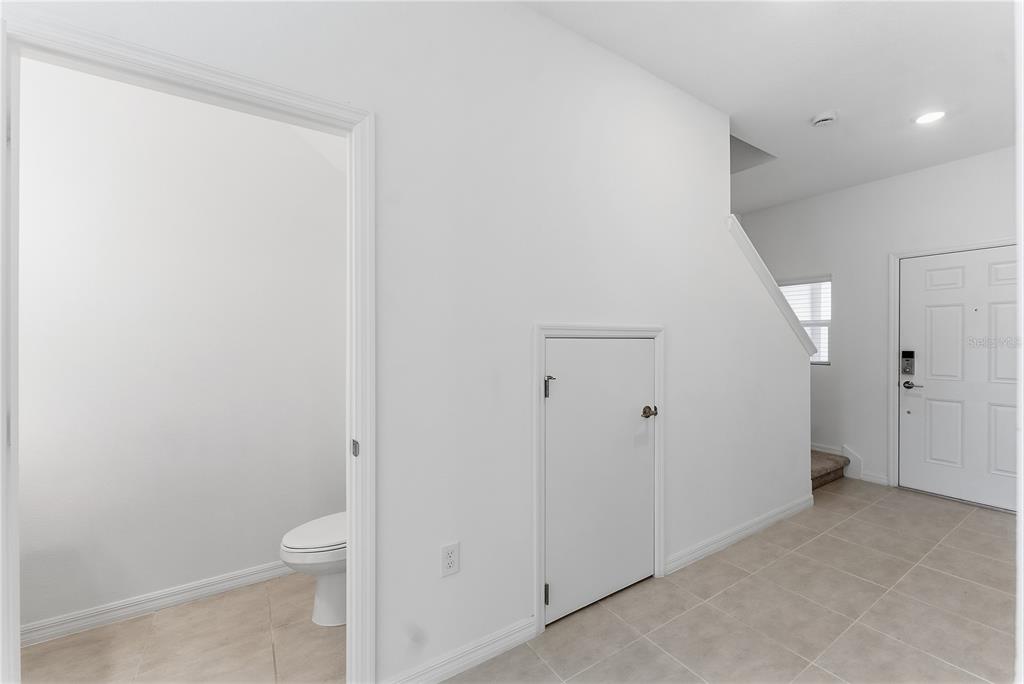 A tiled entryway features a small storage door under the stairs and a nearby bathroom — 1406 ANCHOR BEND WAY, KISSIMMEE, FL