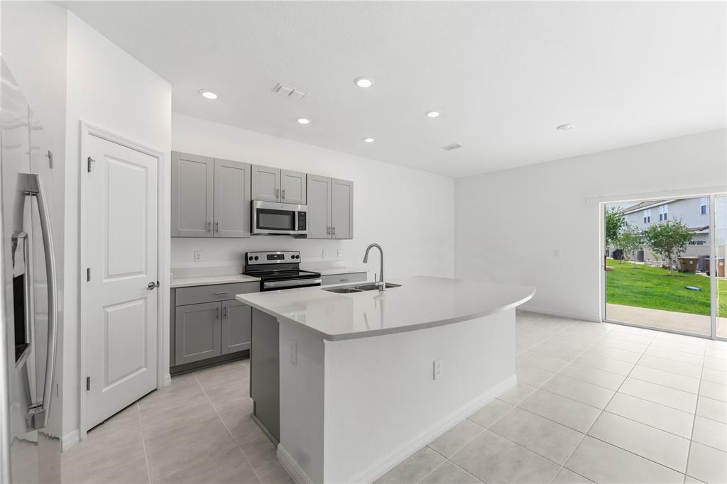 A kitchen features gray cabinets, a white quartz island, stainless steel appliances, and tile flooring — 1406 ANCHOR BEND WAY, KISSIMMEE, FL