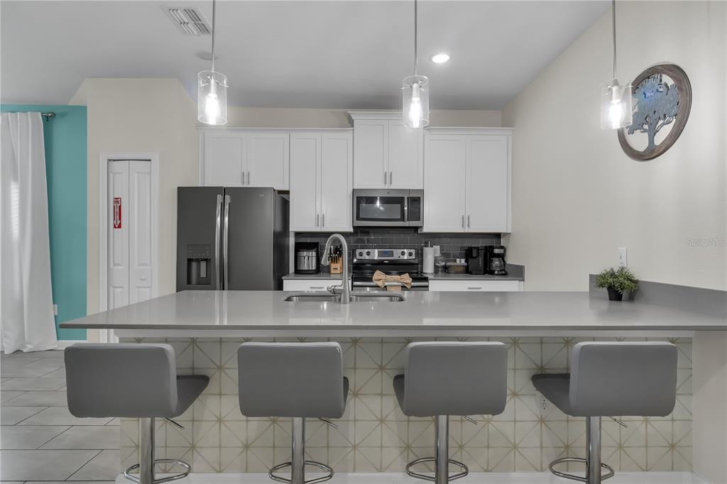 A modern kitchen features white cabinets, stainless steel appliances, a gray island, and four stools — 448 OCEAN COURSE AVENUE, DAVENPORT, FL