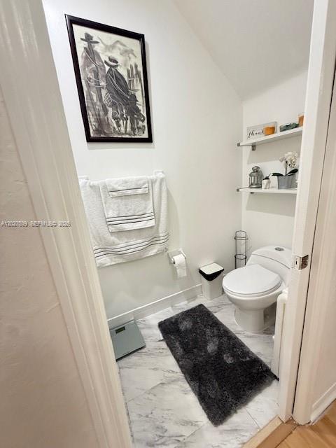 A small bathroom features a toilet, white walls, marble-look flooring, and wall-mounted shelving — 5610 NW 114th Pl # 202, Doral FL 33178, DORAL, FL