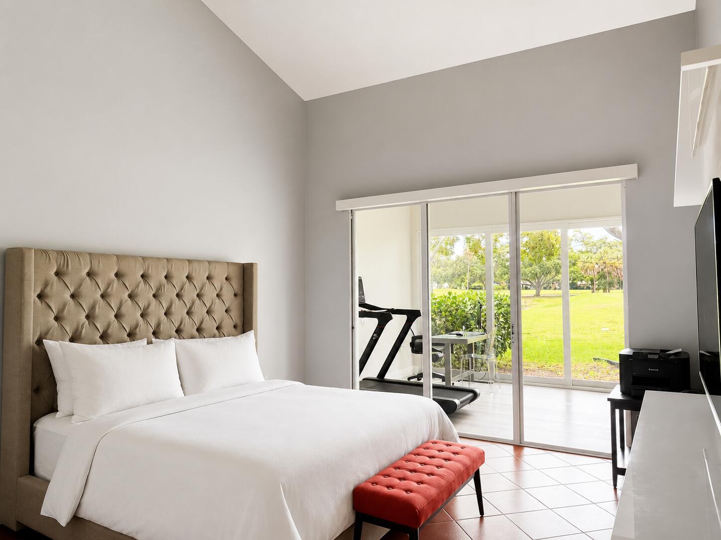A bedroom with a tufted headboard, red bench, and sliding doors opening to a patio — 4103 Carriage Drive # H4, Pompano Beach FL 33069, POMPANO BEACH, FL