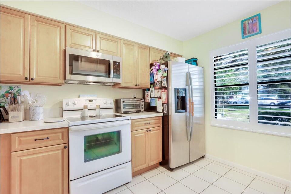 A kitchen features light wood cabinets, white appliances, a stainless steel refrigerator, and tile flooring — 1601 Sabal Ridge Circle # C, Palm Beach Gardens FL 33418, PALM BEACH GARDENS, FL