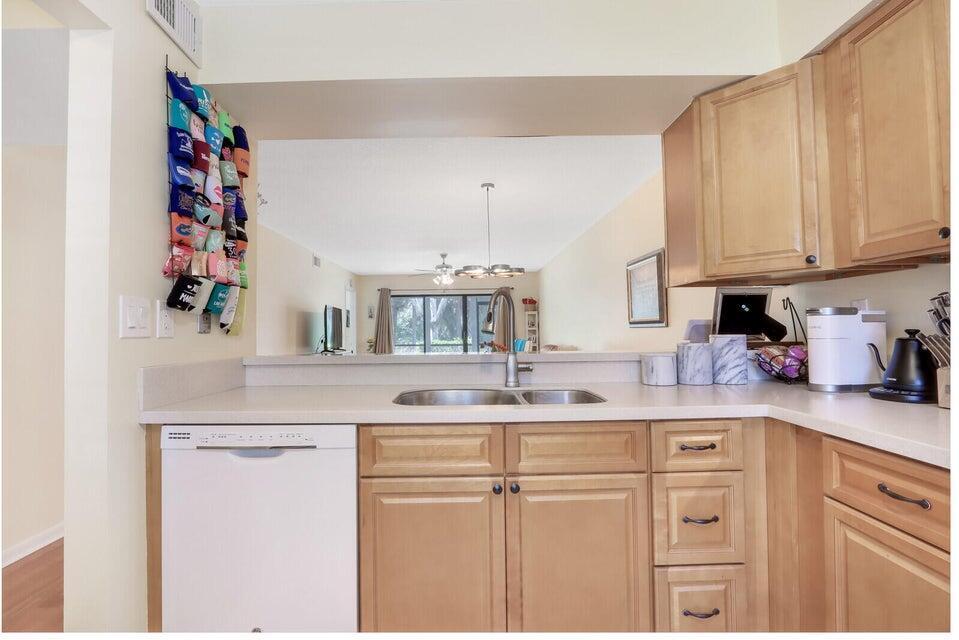 A kitchen features light wood cabinets, a white dishwasher, and a pass-through to the living area — 1601 Sabal Ridge Circle # C, Palm Beach Gardens FL 33418, PALM BEACH GARDENS, FL