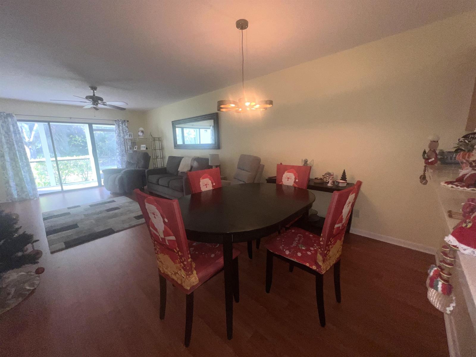 A dining area with a dark wood table and Santa-themed chair covers sits near a living room — 1601 Sabal Ridge Circle # C, Palm Beach Gardens FL 33418, PALM BEACH GARDENS, FL