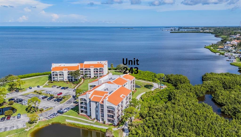 An aerial view shows two multi-story apartment buildings with orange roofs near a large bay — 243 MARINER DRIVE UNIT 243, TARPON SPRINGS, FL