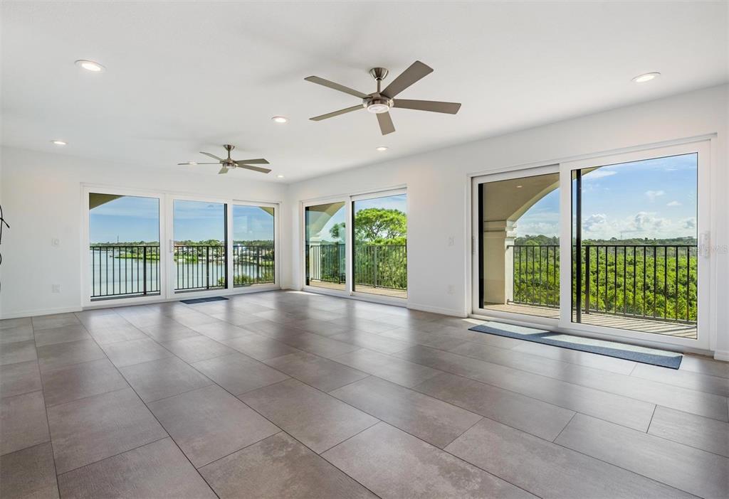 A spacious, empty room features large sliding glass doors, ceiling fans, and gray tile flooring — 243 MARINER DRIVE UNIT 243, TARPON SPRINGS, FL