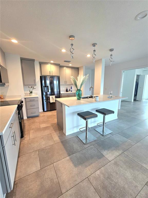 A modern kitchen features gray cabinetry, a central island with bar stools, and tiled flooring — 243 MARINER DRIVE UNIT 243, TARPON SPRINGS, FL
