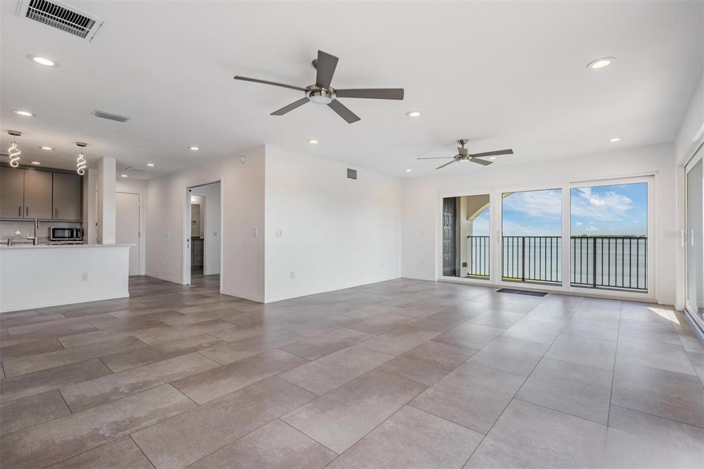An open-concept living area features large gray floor tiles, two ceiling fans, and balcony access — 243 MARINER DRIVE UNIT 243, TARPON SPRINGS, FL