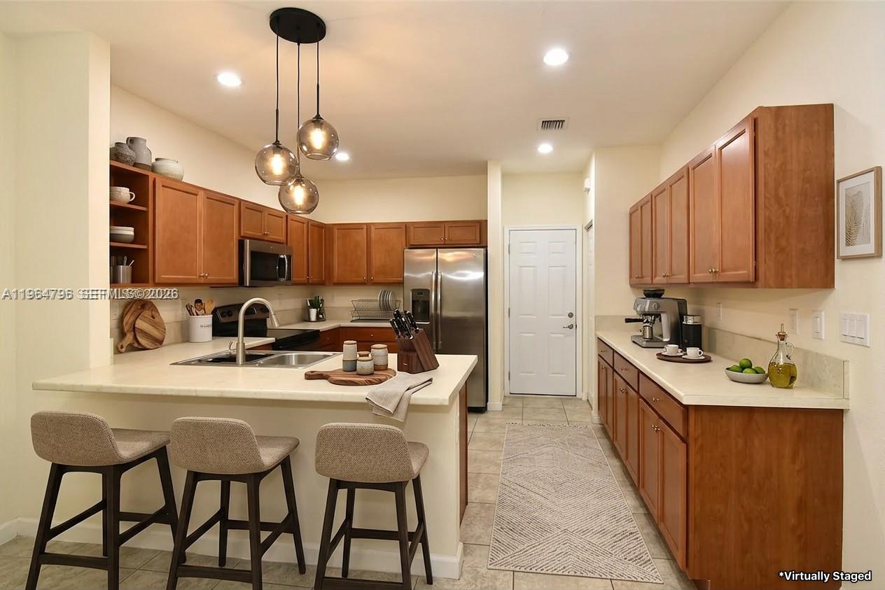 A kitchen with wood cabinets, stainless steel appliances, and a breakfast bar with three stools — 526 SE 35th Ave, Homestead FL 33033, HOMESTEAD, FL
