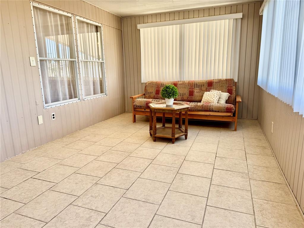 A sunroom features light-colored tile flooring, wood-paneled walls, a futon, and a small wooden table — 340 PEACE MANOR, PALMETTO, FL