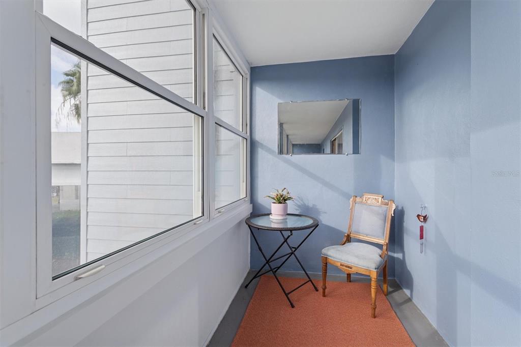 A sunroom features blue walls, a glass-topped table, a wooden chair, and large windows — 841 4TH AVENUE N UNIT 32, ST PETERSBURG, FL