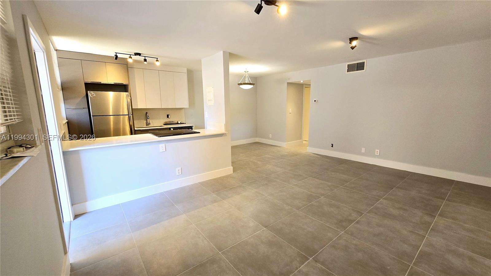 An open-concept kitchen with stainless steel appliances overlooks a tiled living and dining area — 1811 Jefferson St # 202, Hollywood FL 33020, HOLLYWOOD, FL