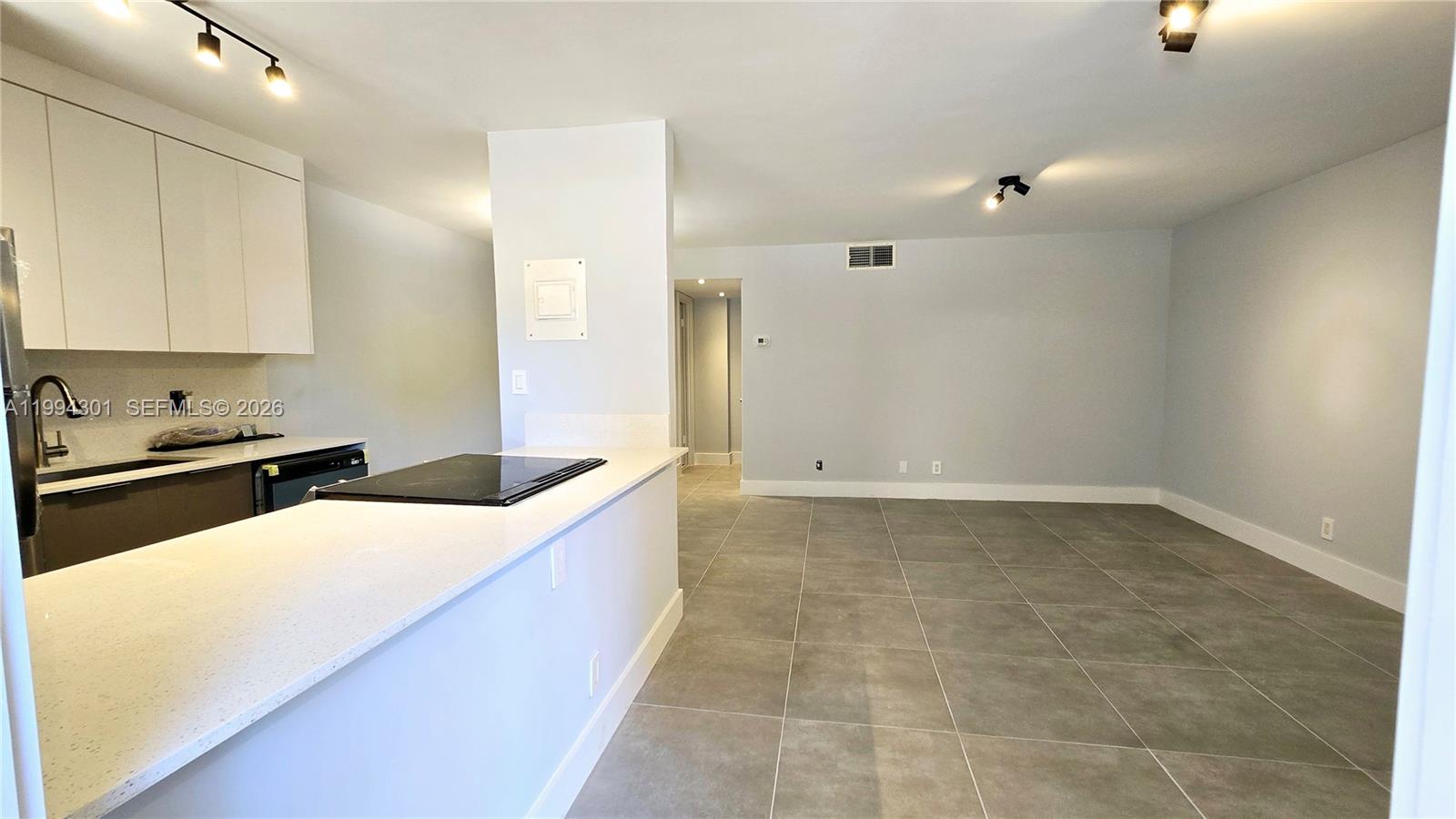 A kitchen with white cabinets and a breakfast bar opens into a tiled living area — 1811 Jefferson St # 202, Hollywood FL 33020, HOLLYWOOD, FL