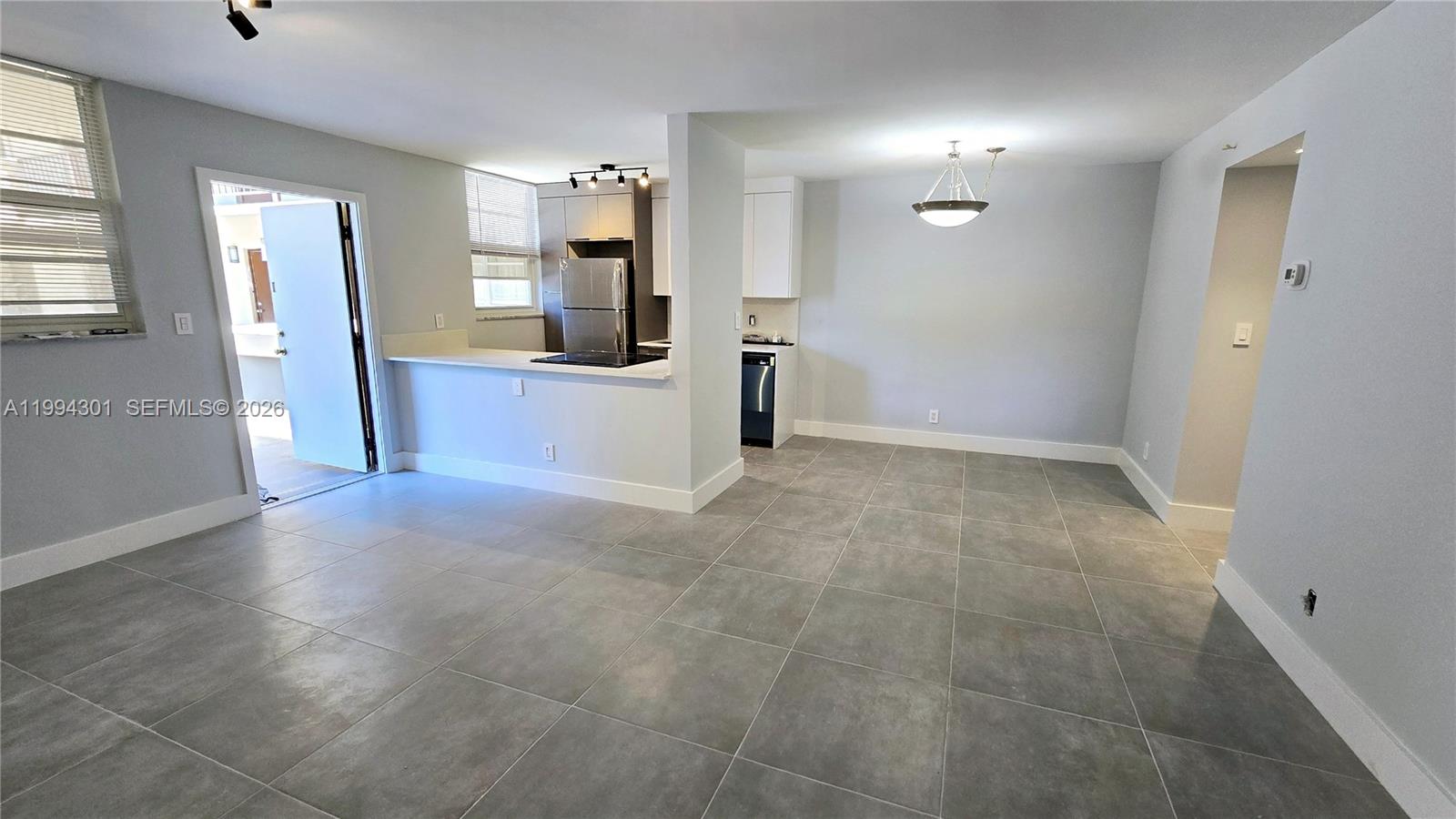 An open-concept kitchen and dining area features gray tile flooring and white cabinetry — 1811 Jefferson St # 202, Hollywood FL 33020, HOLLYWOOD, FL