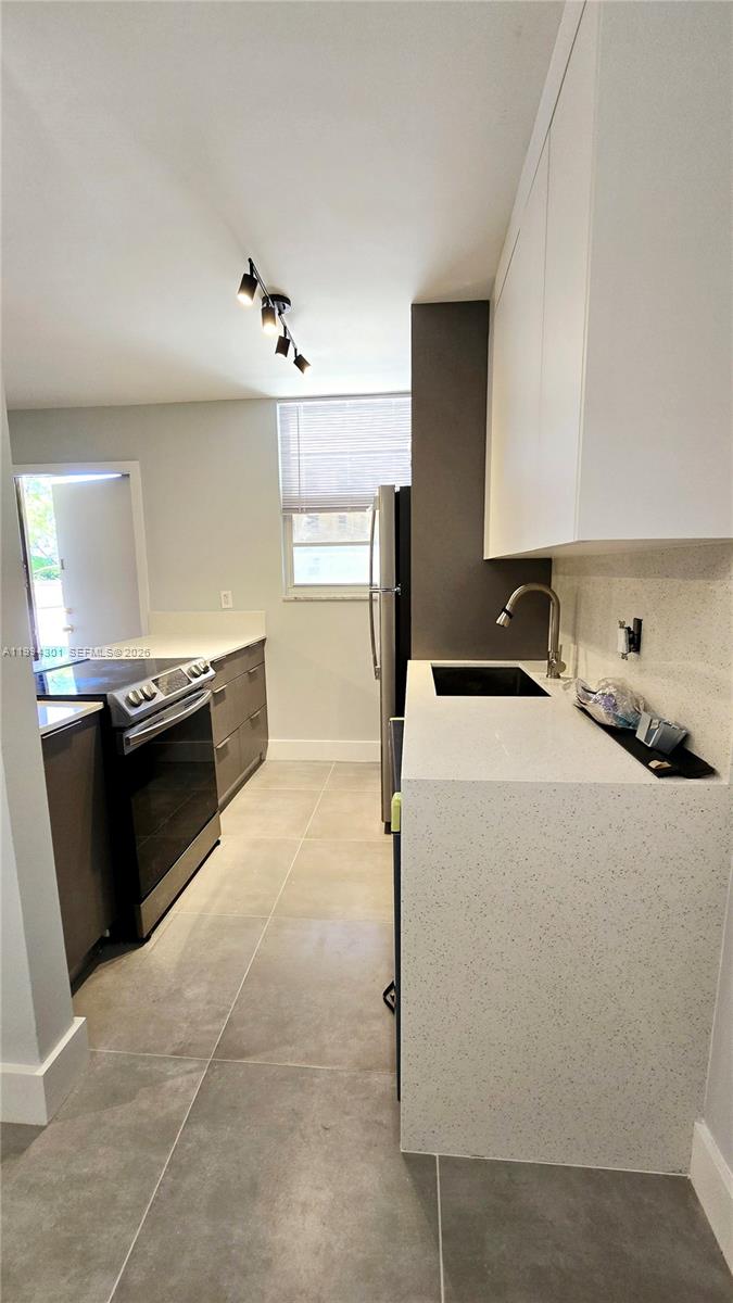 A modern kitchen features white cabinets, quartz countertops, stainless steel appliances, and large floor tiles — 1811 Jefferson St # 202, Hollywood FL 33020, HOLLYWOOD, FL