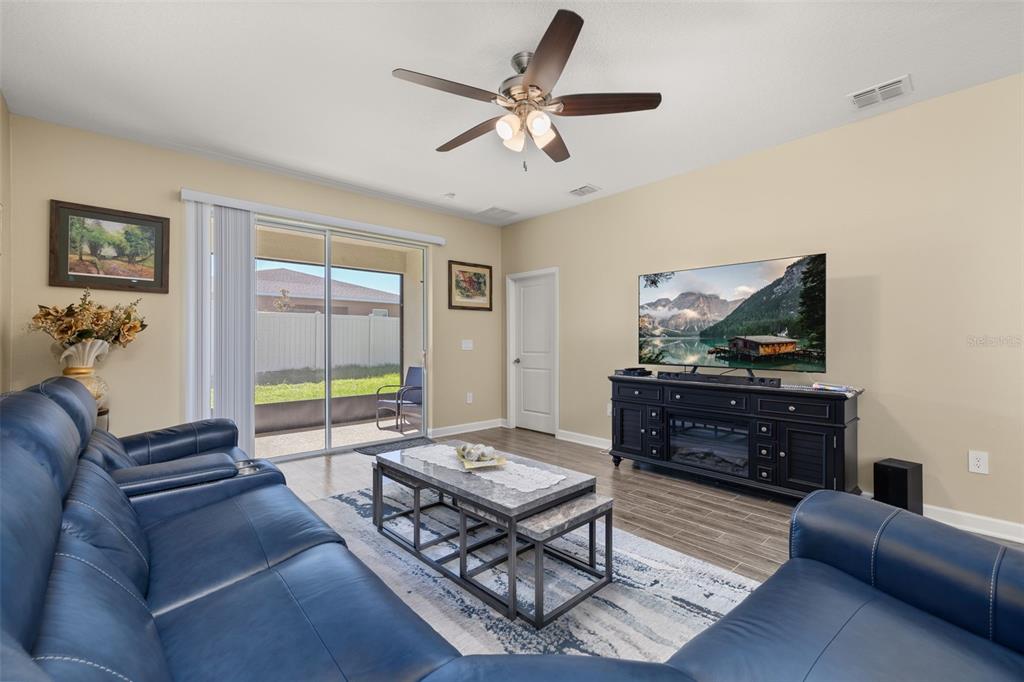 A living room features blue leather sofas, a coffee table, and a television on a console — 1739 GOOD NEIGHBOR LOOP, KISSIMMEE, FL