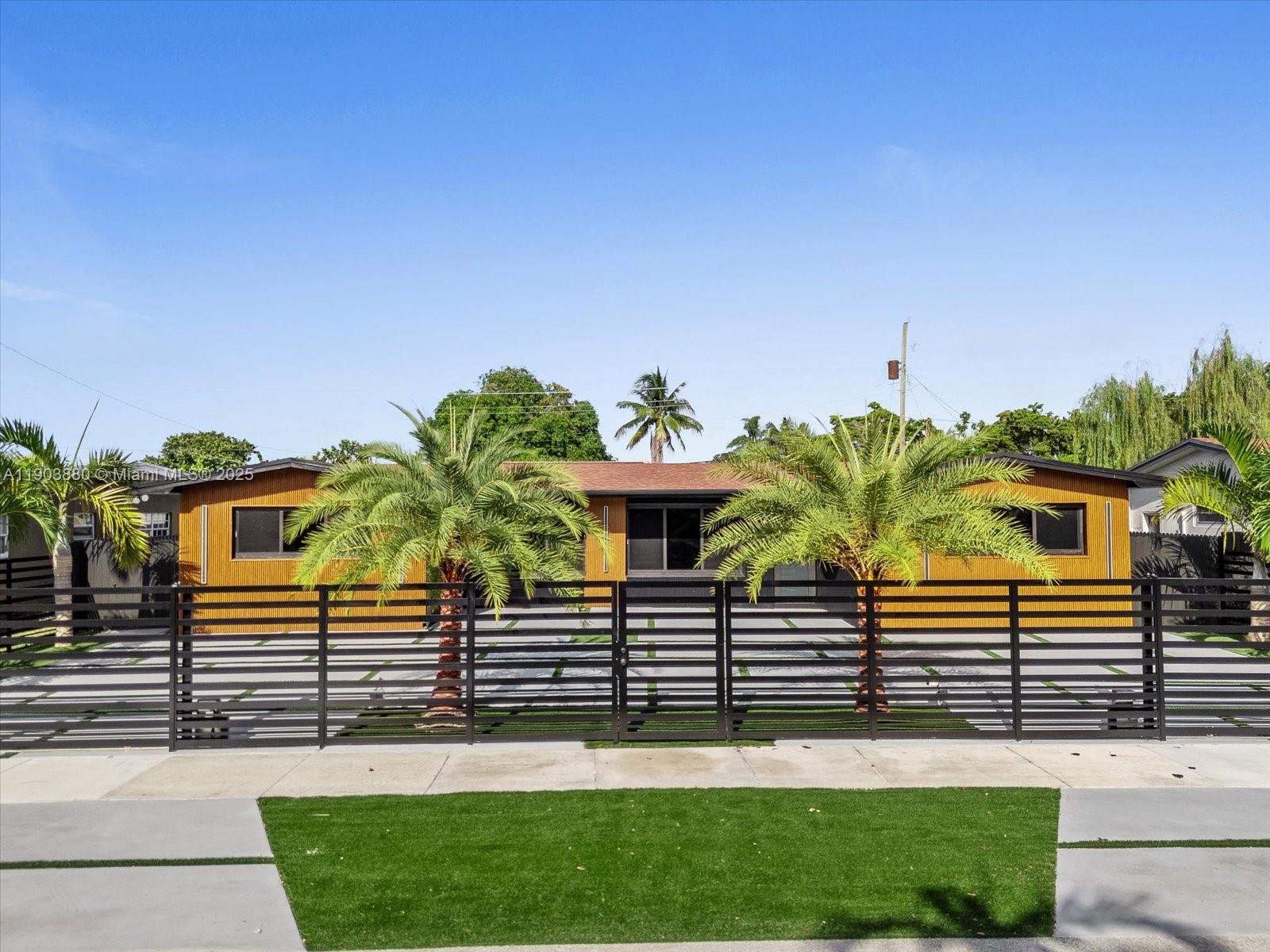 A single-story house with yellow siding and a black fence behind two palm trees — 19511 NE 18th Pl, Miami FL 33179, MIAMI, FL