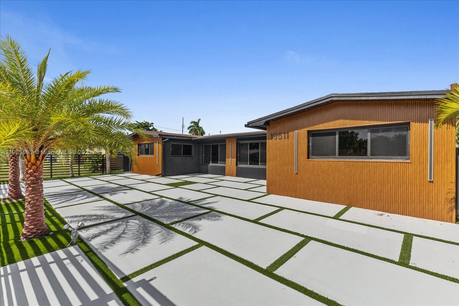 A modern house exterior features wood-paneled walls and a large concrete paver driveway with grass — 19511 NE 18th Pl, Miami FL 33179, MIAMI, FL