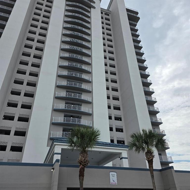 A low-angle view of a tall, multi-story residential building with balconies and two palm trees — 13427 BLUE HERON BEACH DR UNIT 1405, ORLANDO, FL
