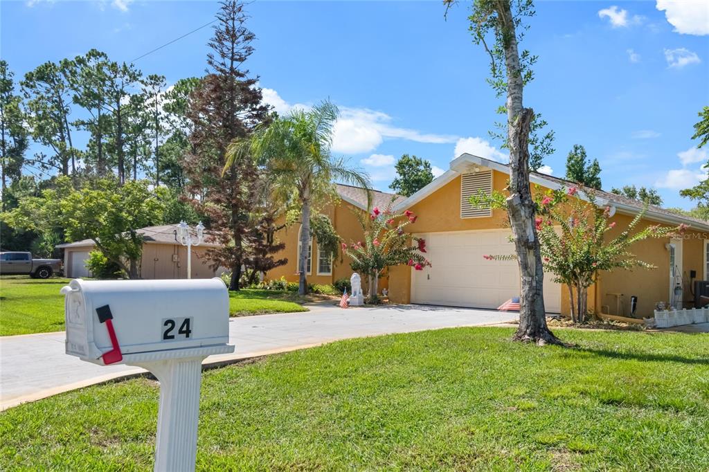 A single-story yellow house with a two-car garage and a mailbox labeled 24 — 24 FOSTER LANE, PALM COAST, FL