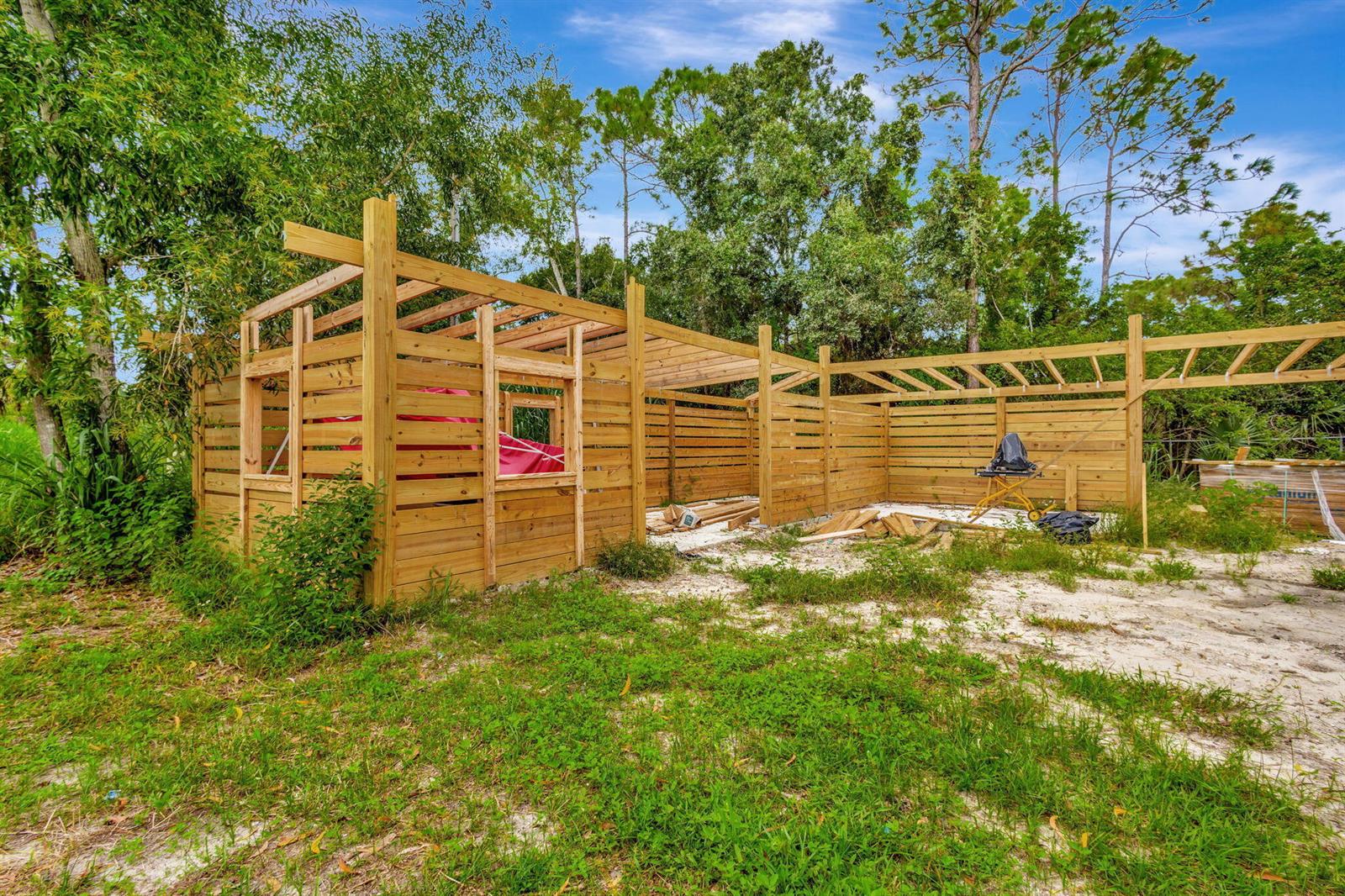 An unfinished wooden structure with horizontal slat walls stands in a grassy, wooded area — 15532 43rd Road N, FL 33470, FL