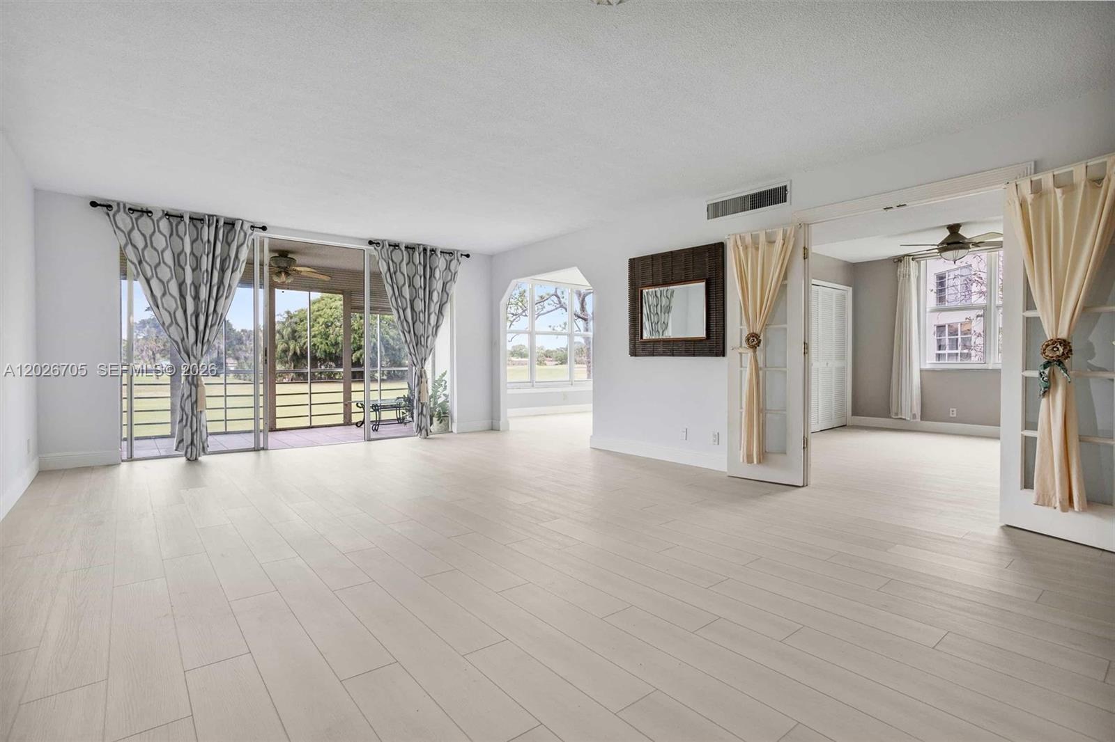 A bright living room features light wood-look flooring, sliding glass doors, and an adjacent room — 2651 S Course Dr # 201, Pompano Beach FL 33069, POMPANO BEACH, FL