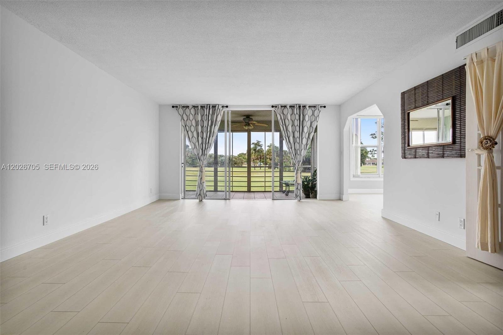 A bright living room features light wood-look flooring, white walls, and a sliding glass door — 2651 S Course Dr # 201, Pompano Beach FL 33069, POMPANO BEACH, FL