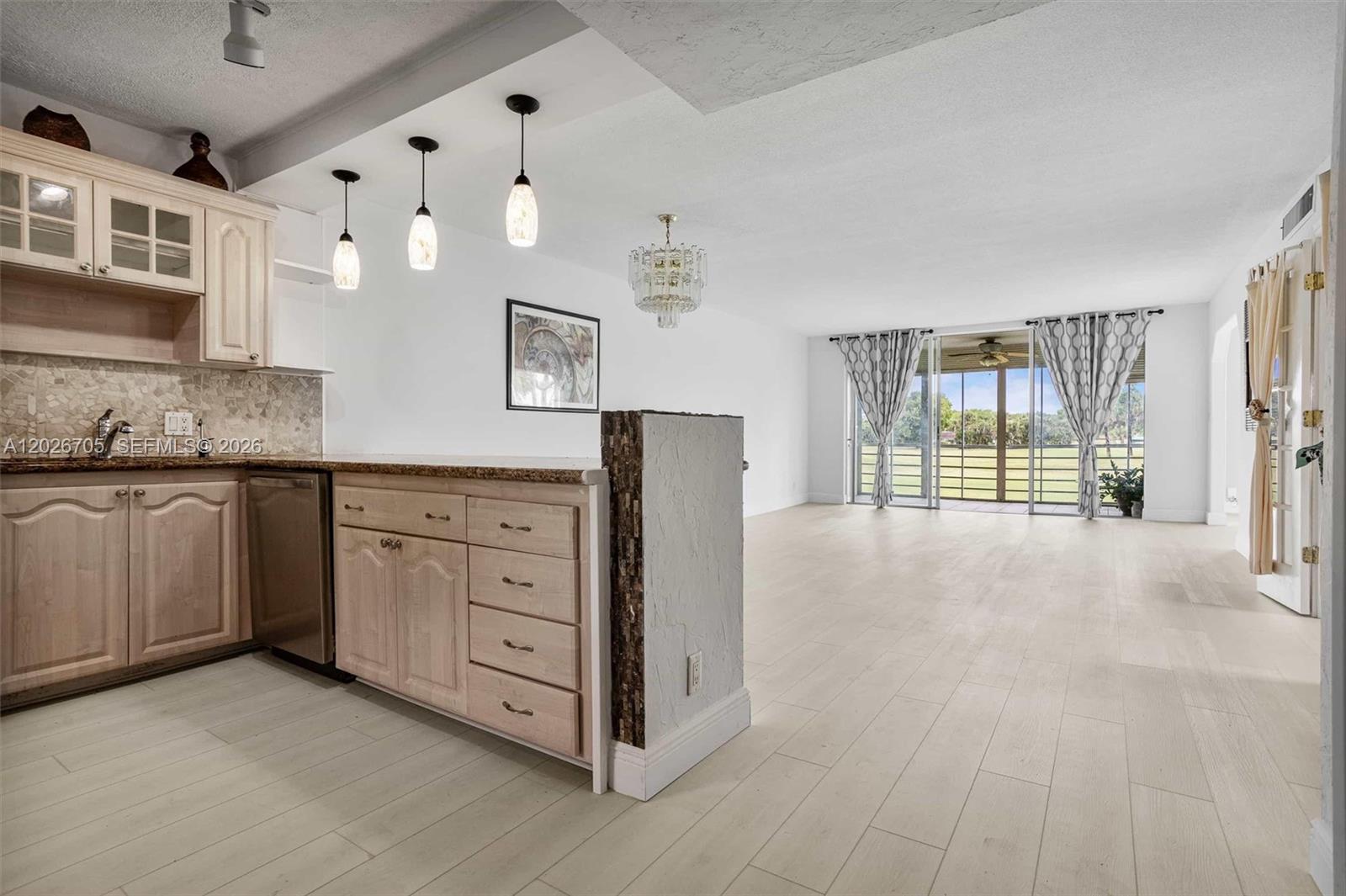 A kitchen with light wood cabinets and a breakfast bar opens into a spacious living area — 2651 S Course Dr # 201, Pompano Beach FL 33069, POMPANO BEACH, FL