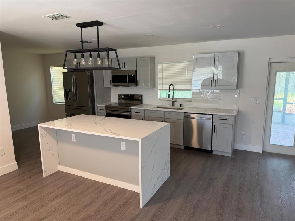 A modern kitchen features a waterfall island, gray cabinetry, stainless steel appliances, and wood flooring — 3621 HAWTHORNE LANE, WINTER PARK, FL