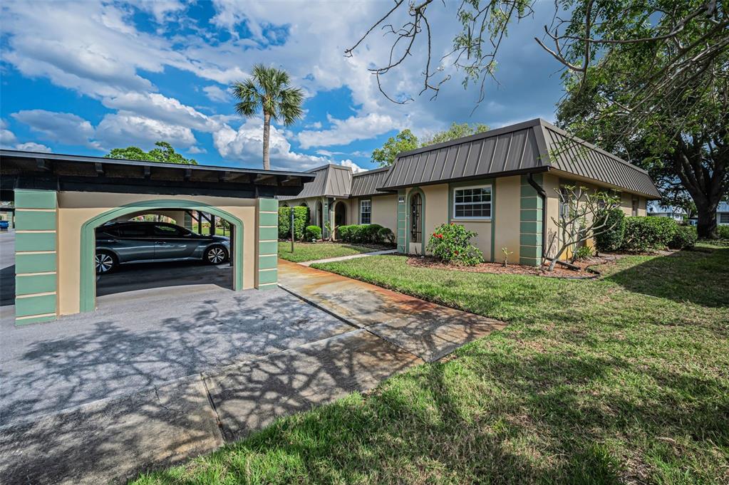 A covered carport with a dark wooden frame sits in front of a tan building — 4200 HAMPTON DRIVE, NEW PORT RICHEY, FL