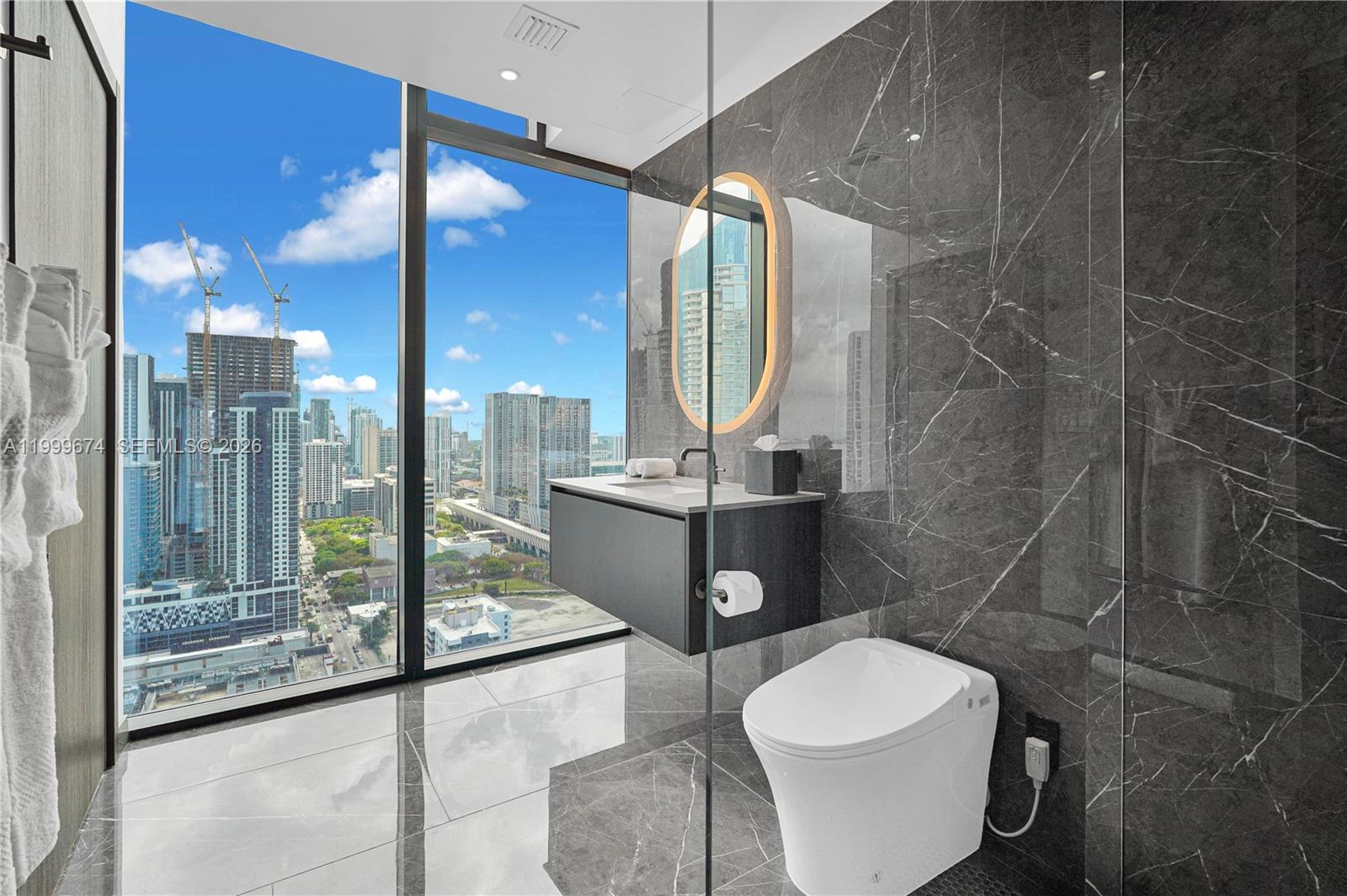 A modern bathroom features dark marble walls, a floating vanity, and floor-to-ceiling city views — 20 NE 11th St # 3110, Miami FL 33132, MIAMI, FL