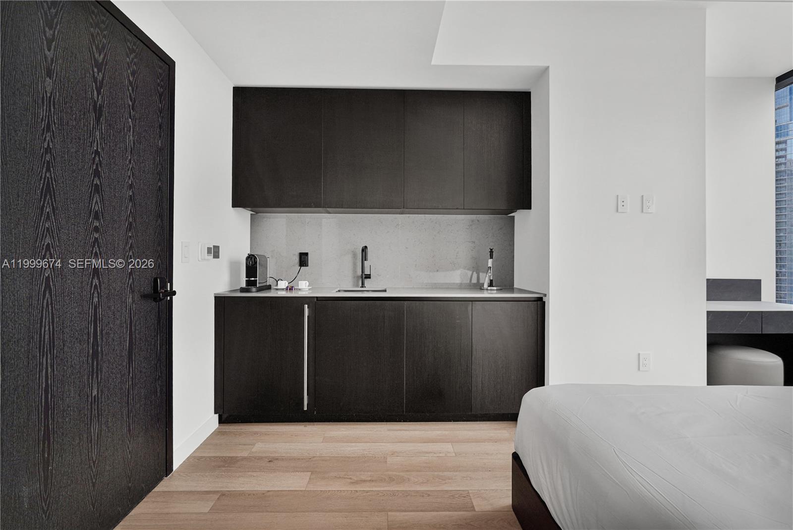 A modern kitchenette features dark wood cabinetry, a light stone backsplash, and a sink — 20 NE 11th St # 3110, Miami FL 33132, MIAMI, FL