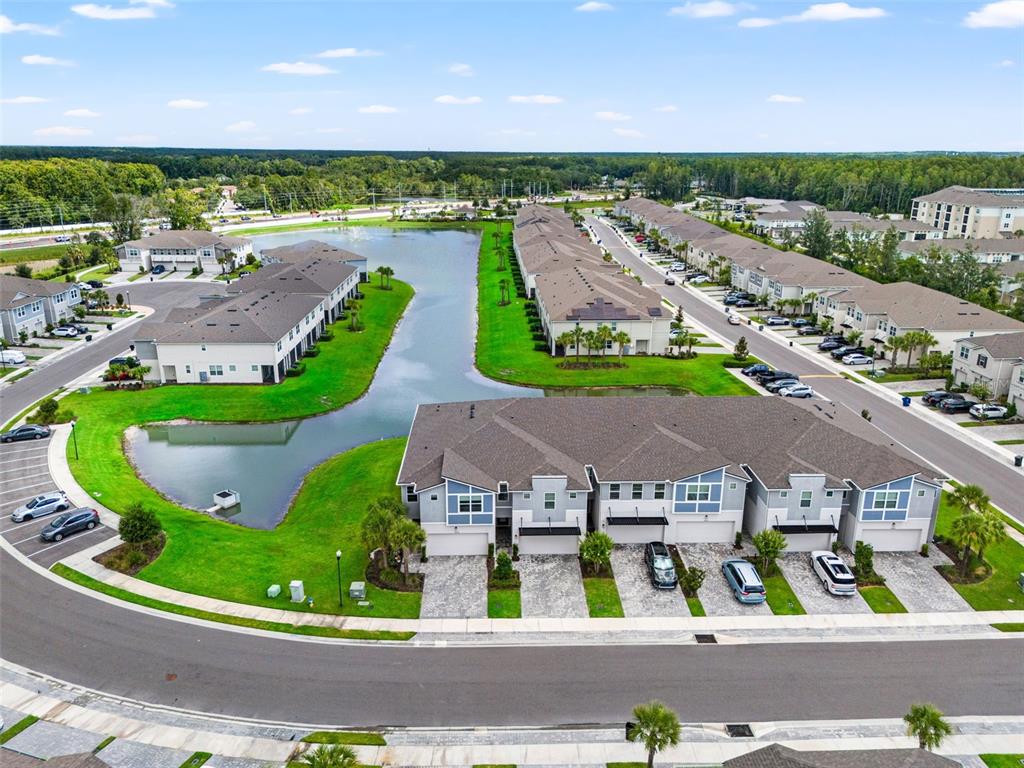 An aerial view shows multiple multi-family residential buildings surrounding a central pond and green space — 26069 WOVEN WICKER BEND, LUTZ, FL