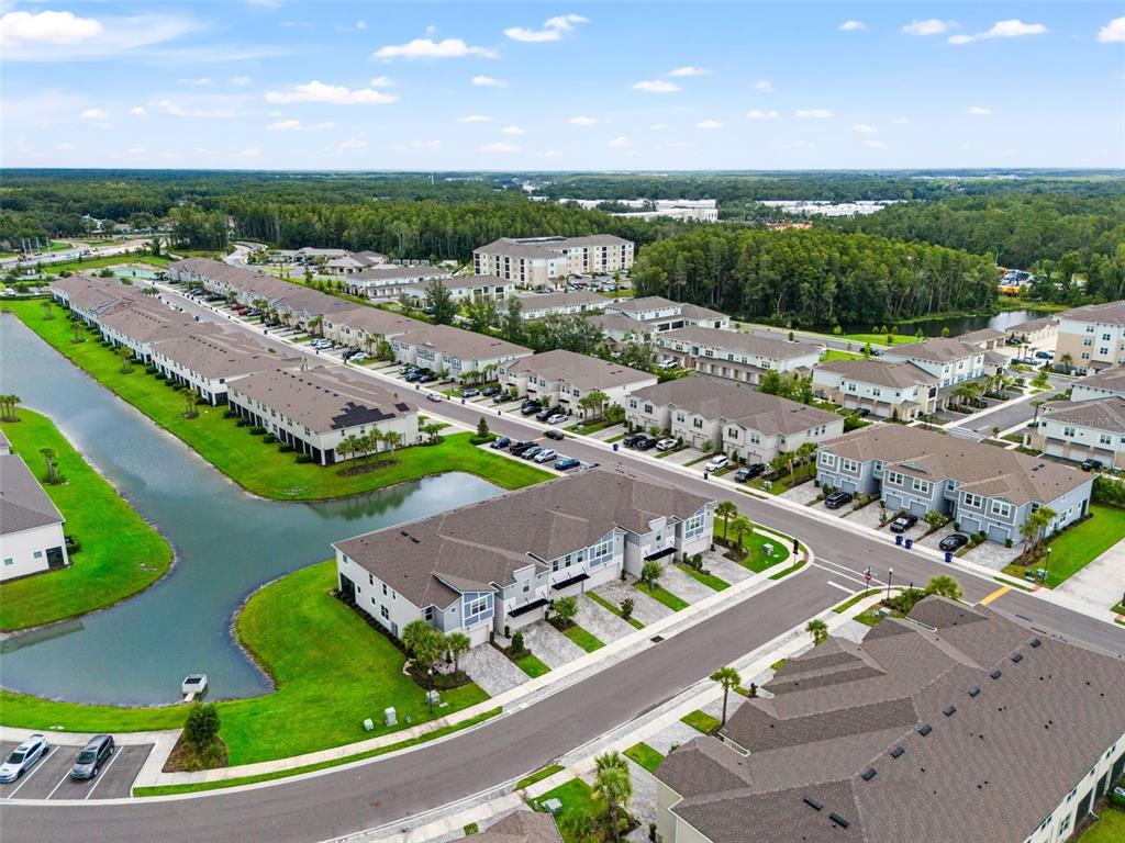 An aerial view shows a residential complex with townhouses, a pond, and paved streets — 26069 WOVEN WICKER BEND, LUTZ, FL