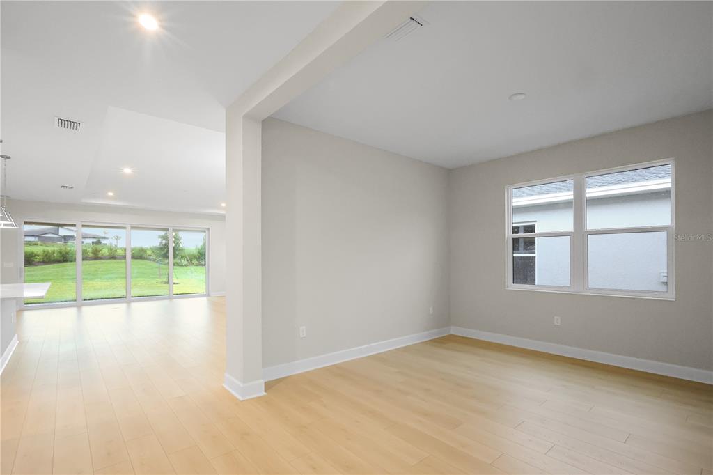 An interior view of a room with light wood flooring, neutral walls, and large windows — 1620 BELLAGIO LOOP, TAVARES, FL