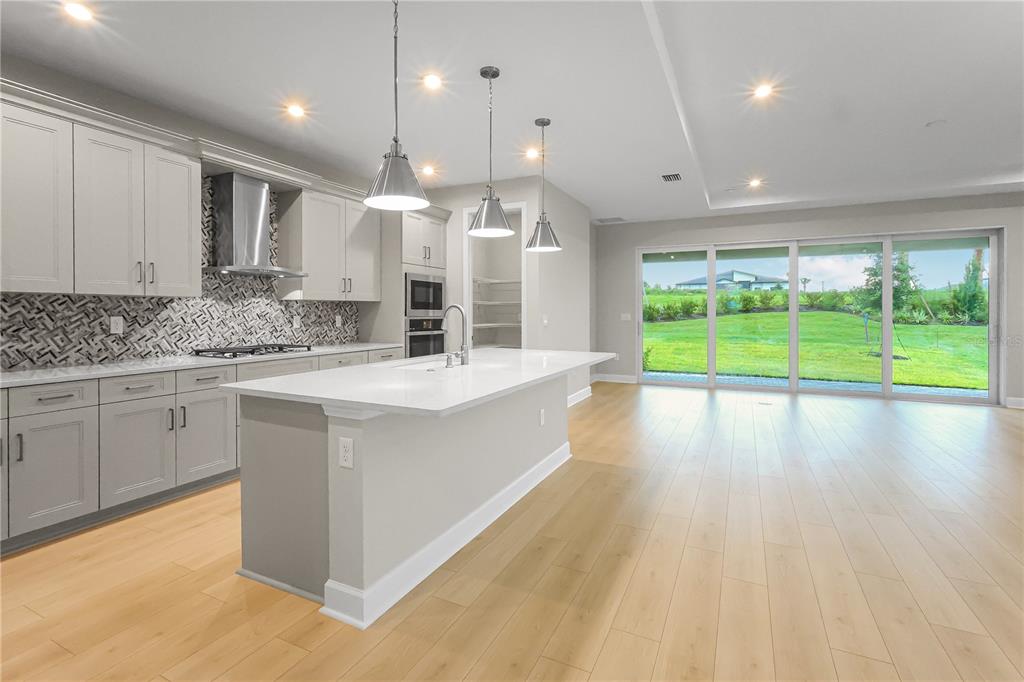 A modern kitchen features light gray cabinets, a white quartz island, and large sliding glass doors — 1620 BELLAGIO LOOP, TAVARES, FL