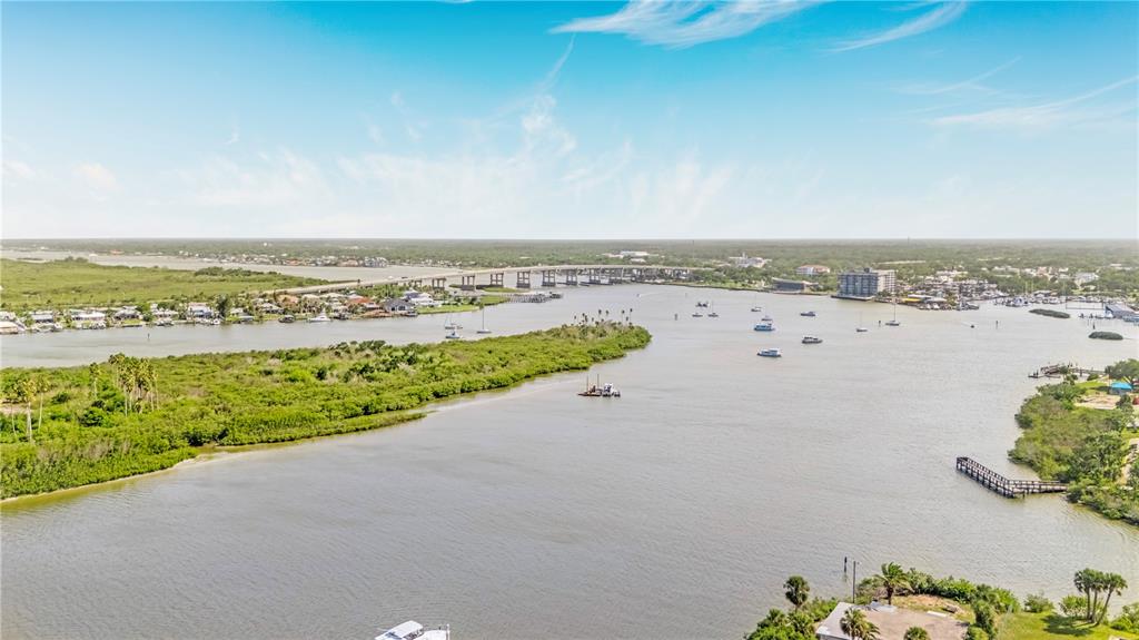An aerial view shows a wide river with boats, a bridge, and surrounding coastal vegetation — 14 OLD FEGER DRIVE, NEW SMYRNA BEACH, FL