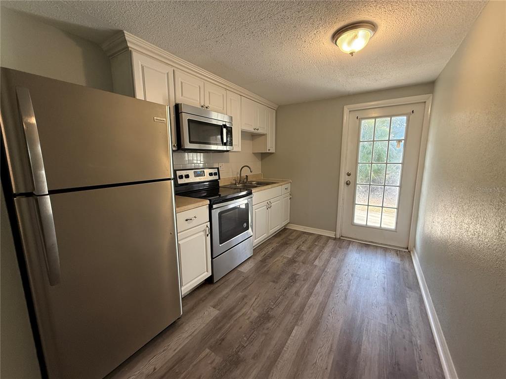 A kitchen features stainless steel appliances, white cabinetry, light countertops, and wood-look flooring — 350 ELMSTREET COURT UNIT 6, ENGLEWOOD, FL