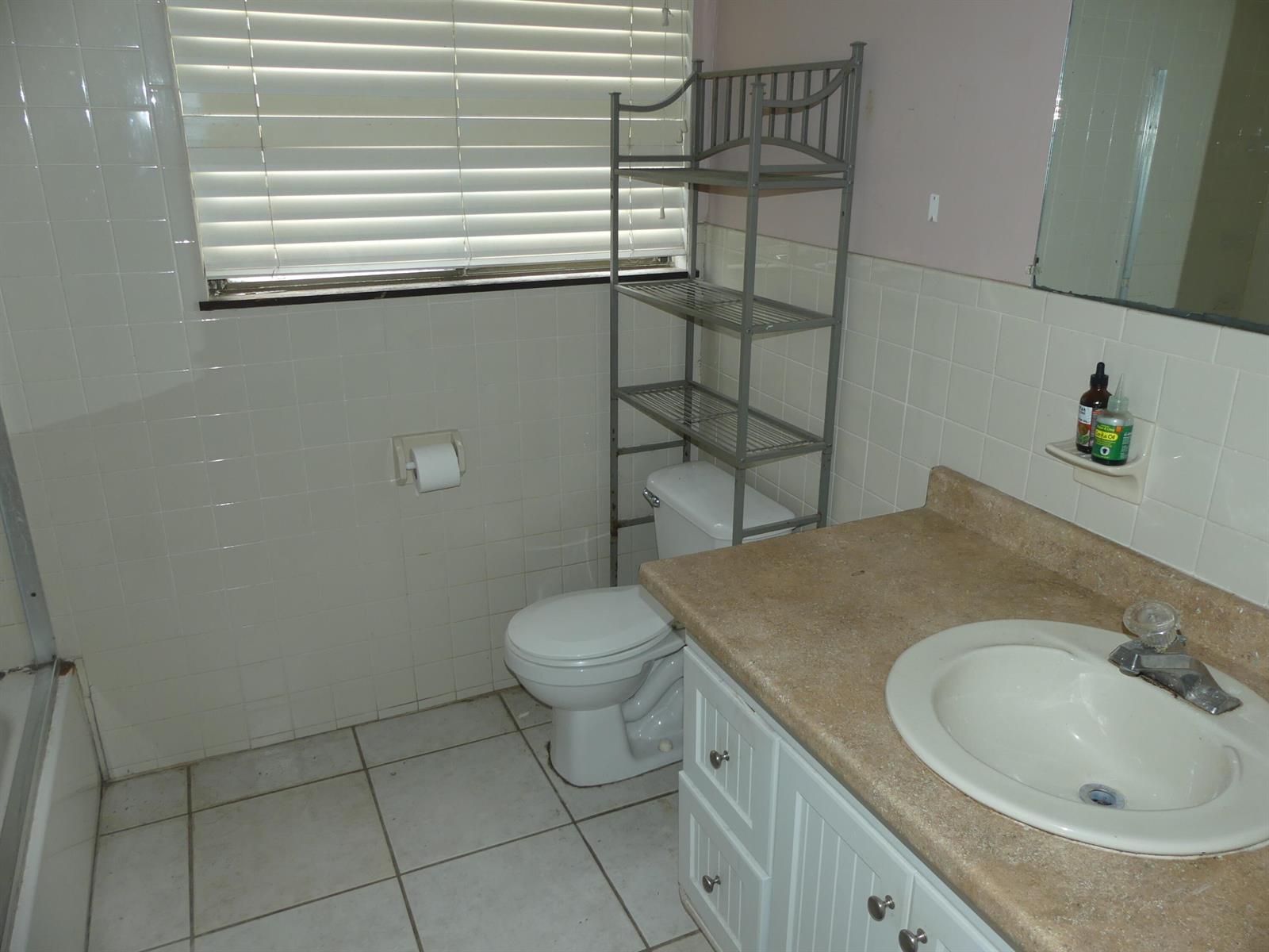 A bathroom features a white vanity, a toilet with a metal storage rack, and tiled walls — 6665 Rigger Road, Lake Worth FL 33462, LAKE WORTH, FL