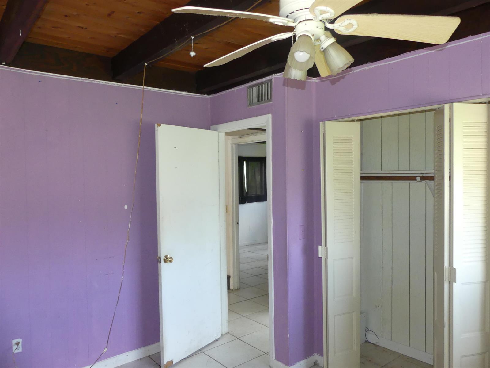 A bedroom with purple walls, a wood-beamed ceiling, a ceiling fan, and two white doors — 6665 Rigger Road, Lake Worth FL 33462, LAKE WORTH, FL