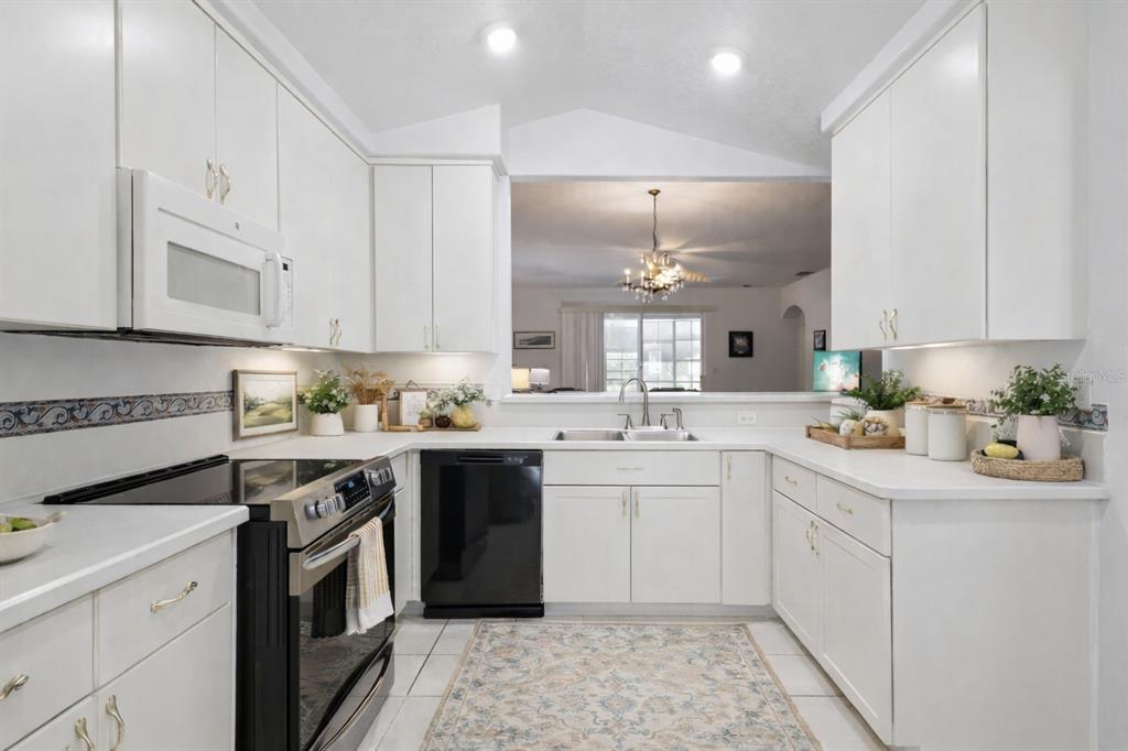 A white kitchen features black appliances, light countertops, and a pass-through window to the living area — 5964 BRITTANIA BOULEVARD, TAVARES, FL