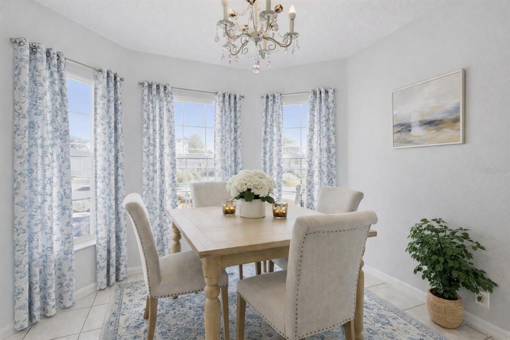 A dining area features a wooden table, four upholstered chairs, blue floral curtains, and a chandelier — 5964 BRITTANIA BOULEVARD, TAVARES, FL