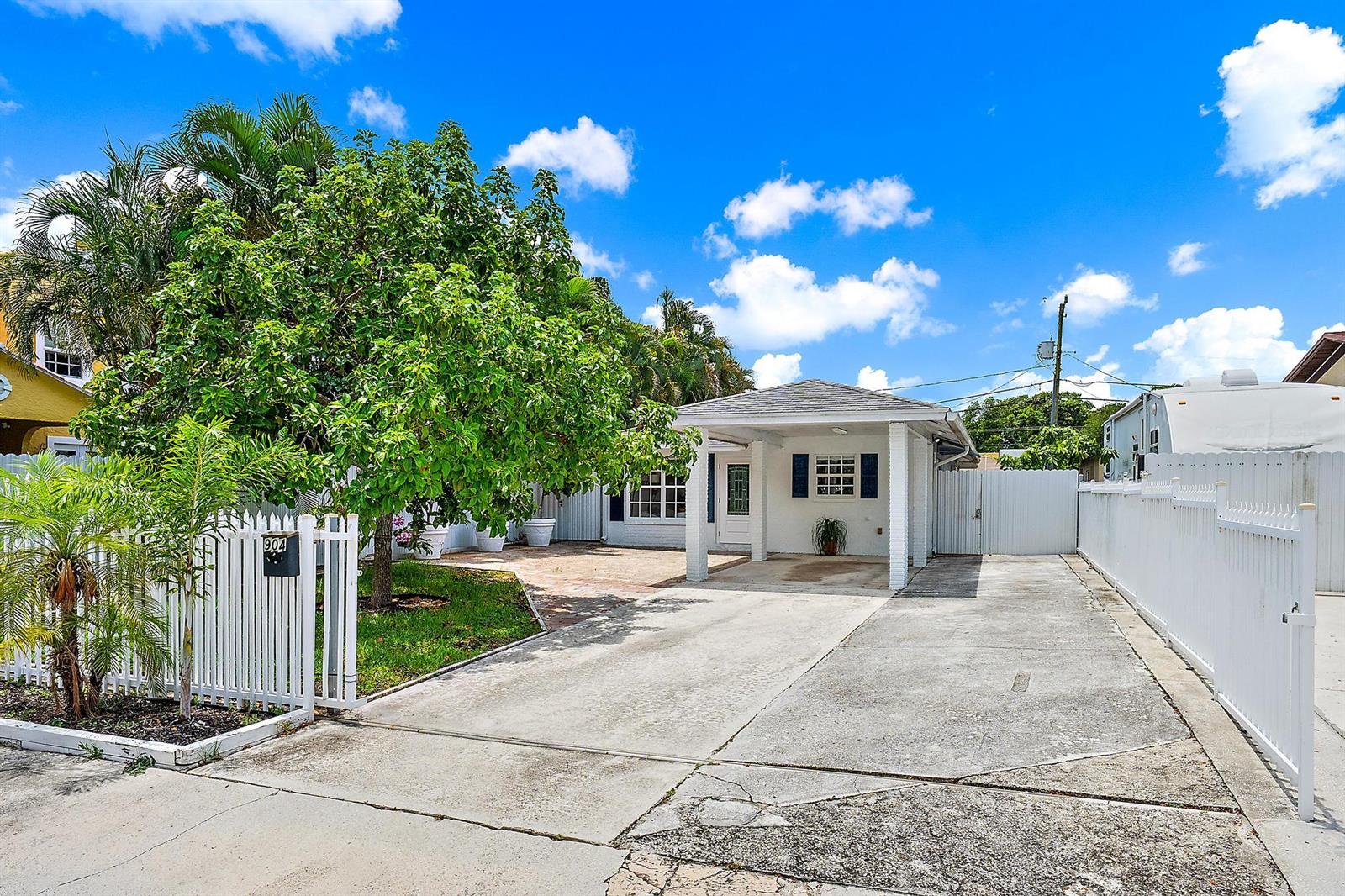 A white single-story house features a concrete driveway, a carport, and a white picket fence — 904 Ortega Road, West Palm Beach FL 33405, WEST PALM BEACH, FL