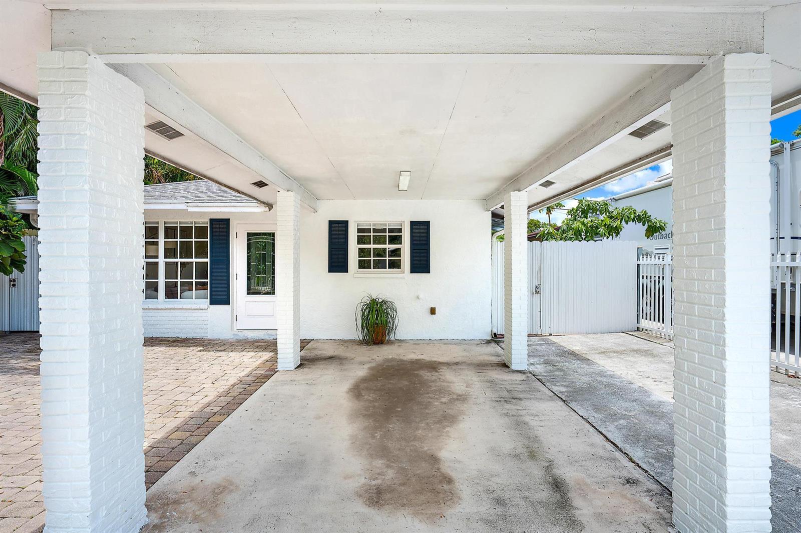 A white carport with brick pillars leads to a house entrance and a paved driveway — 904 Ortega Road, West Palm Beach FL 33405, WEST PALM BEACH, FL