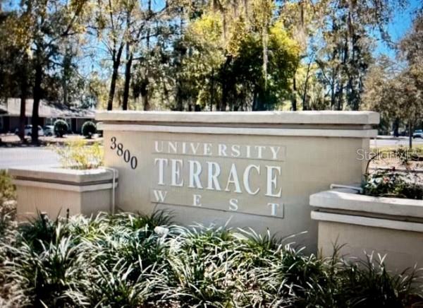 A beige monument sign for University Terrace West stands outdoors surrounded by green landscaping — 3800 SW 20TH AVENUE UNIT 306, GAINESVILLE, FL