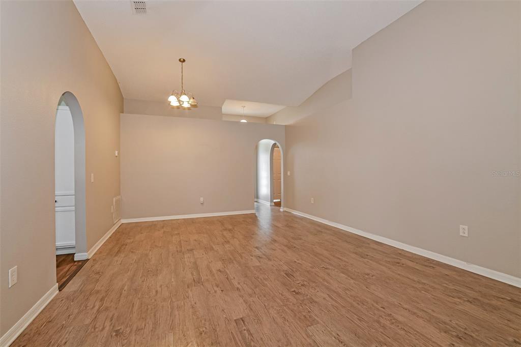 An empty room with light wood-look flooring, beige walls, and two arched doorways — 207 RONALDALE AVENUE, HAINES CITY, FL